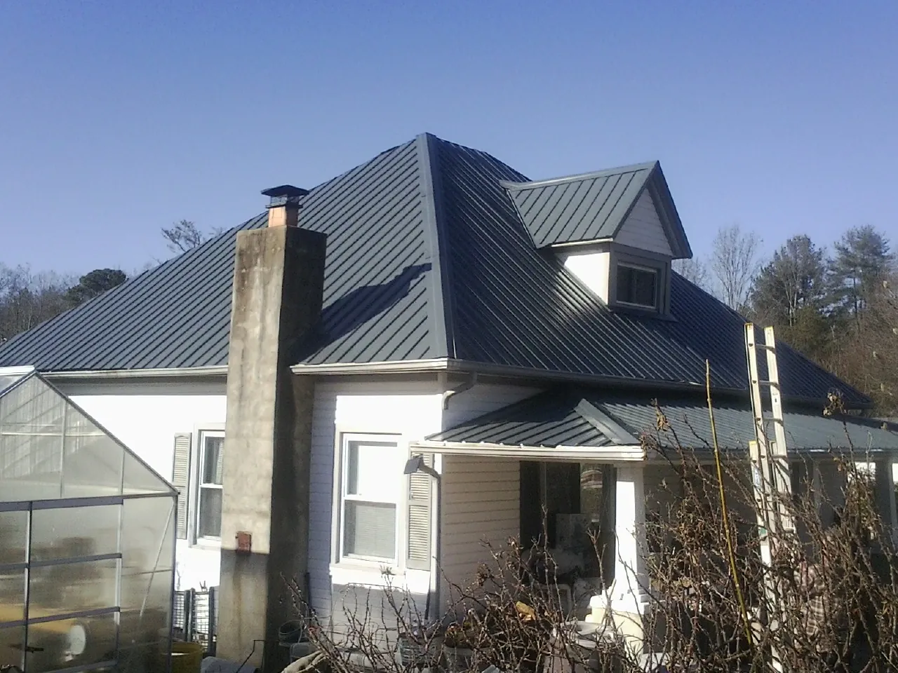 Dark blue standing seam metal roof on a white farmhouse with dormer — Slate & Tile Roof Repair by Roofing Brothers in Blackstock