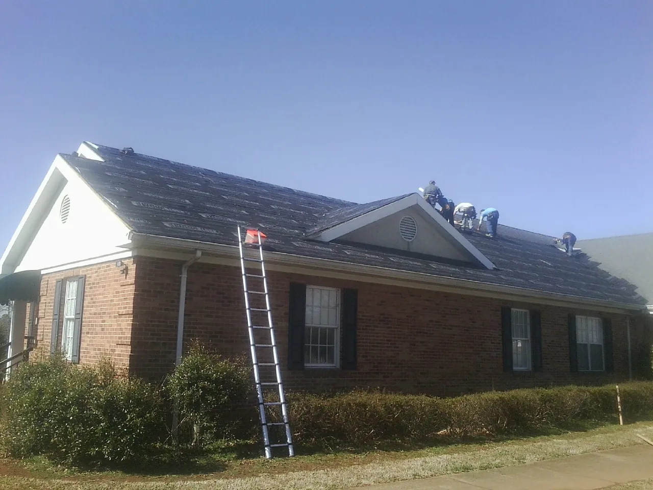 Crew tearing shingles off a brick ranch roof with a ladder set — Metal Roof Repair work by our crew in Blackstock