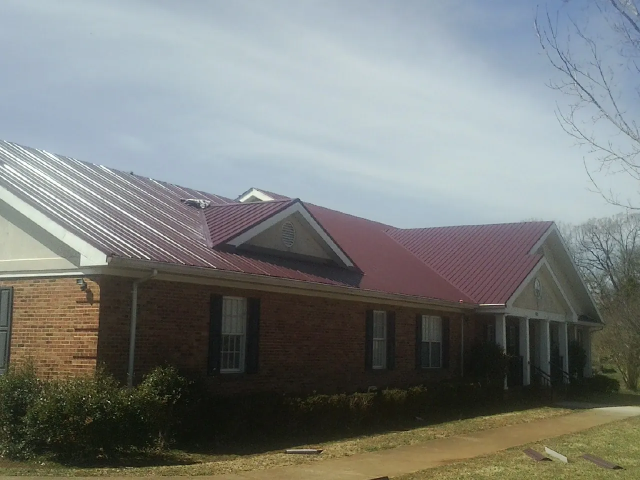 Red metal roof with gabled entries on a long brick building, from a Hail Damage Roof Repair job in Blackstock