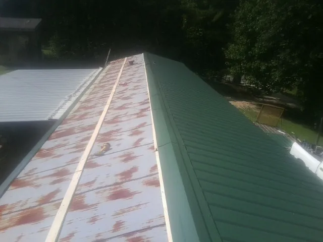 Old rusted panels beside newly installed green metal roofing — Wind Damage Roof Repair by Roofing Brothers in Blackstock