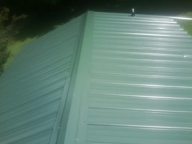 New green metal panels meeting at the ridge of a roof — Flat Roof Repair work by our crew in Blackstock