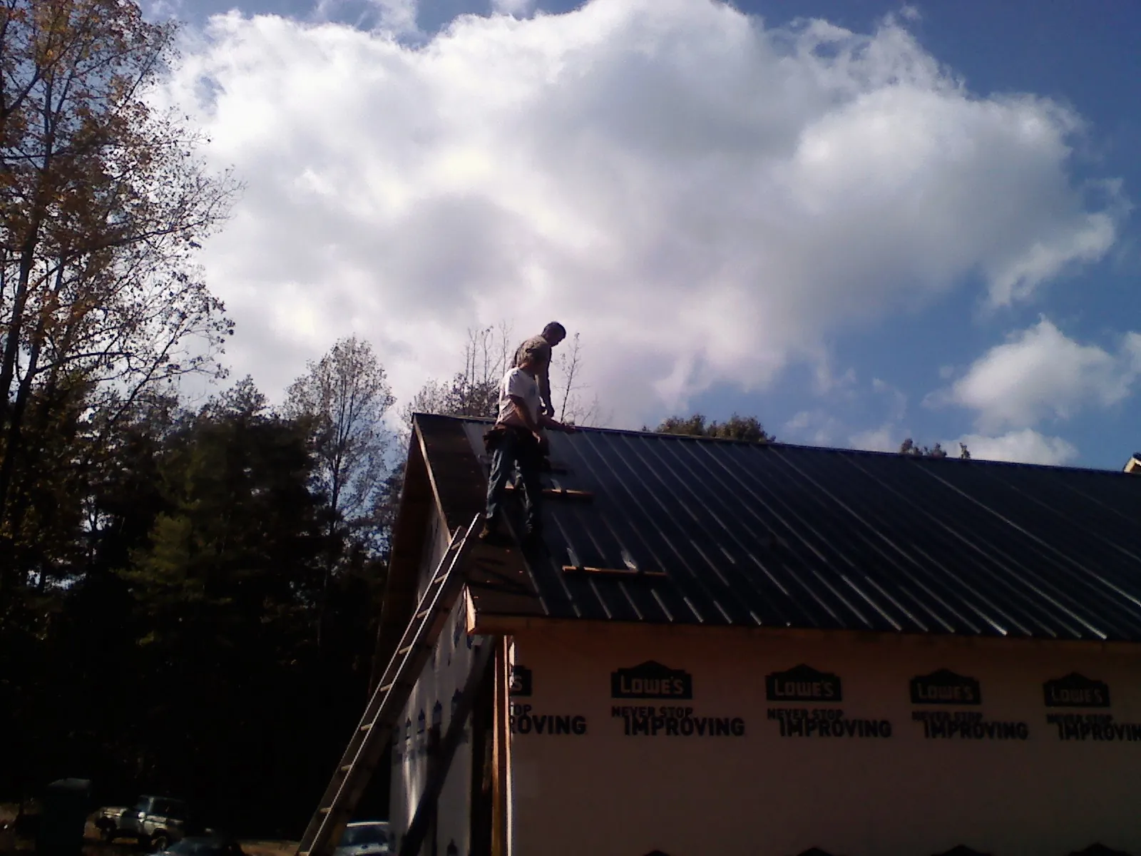 Roofer fastening dark metal panels high against a cloudy sky, from a Roof Inspection job in Blackstock