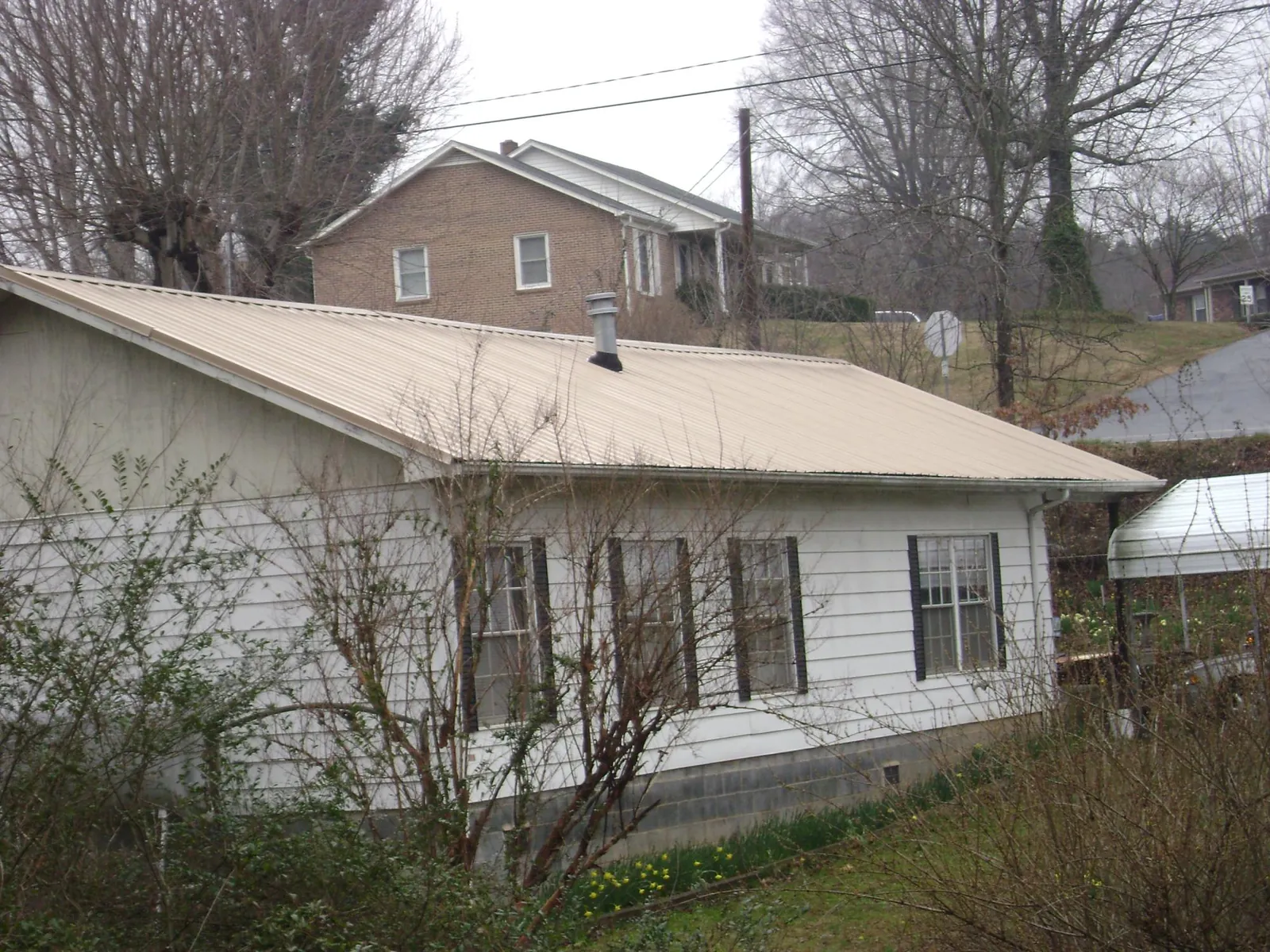 Tan metal roof on a white sided house set into a hillside — Commercial Roofing by Roofing Brothers in Blackstock